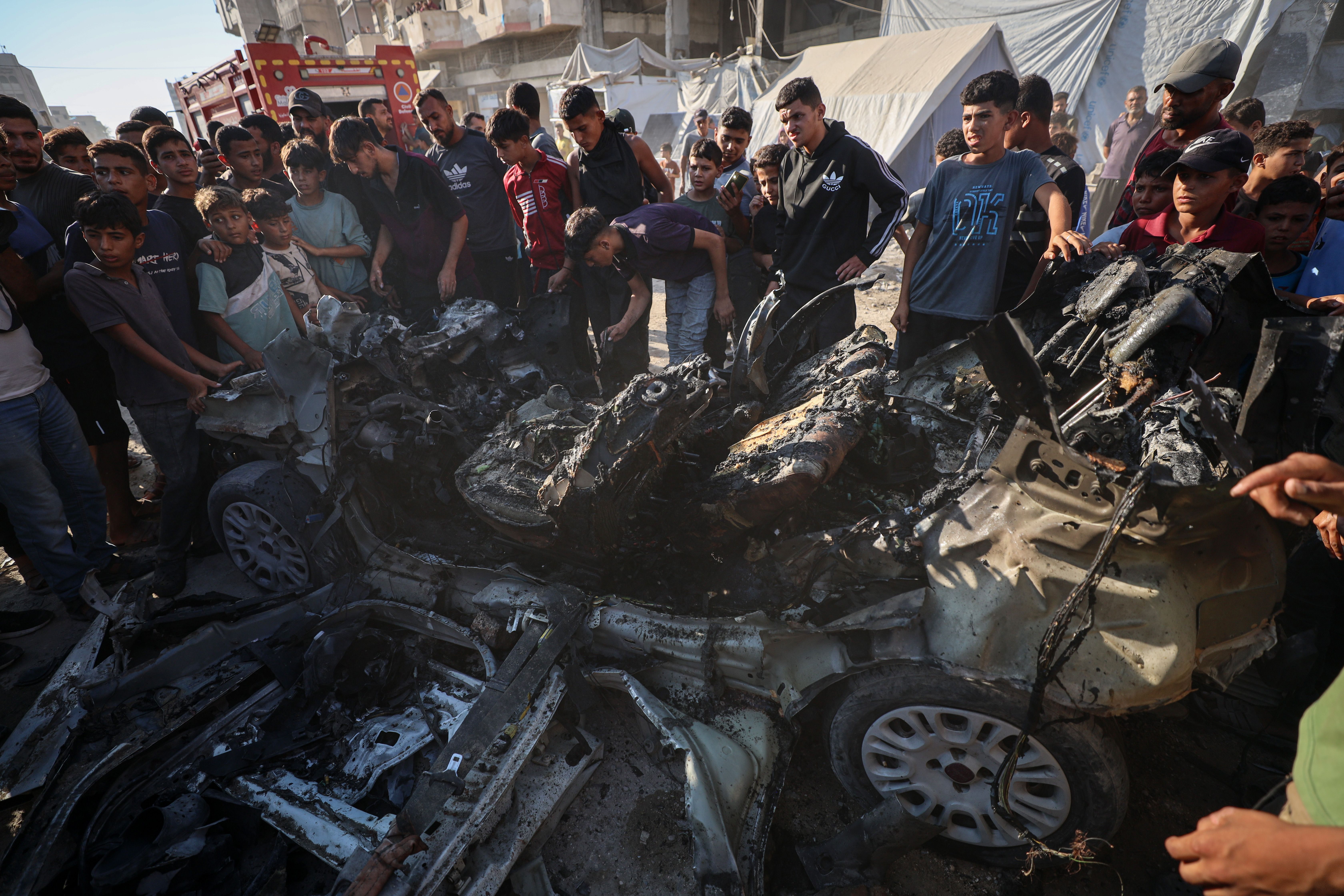 Palestinians gather around destroyed vehicles after Israeli strikes on Gaza