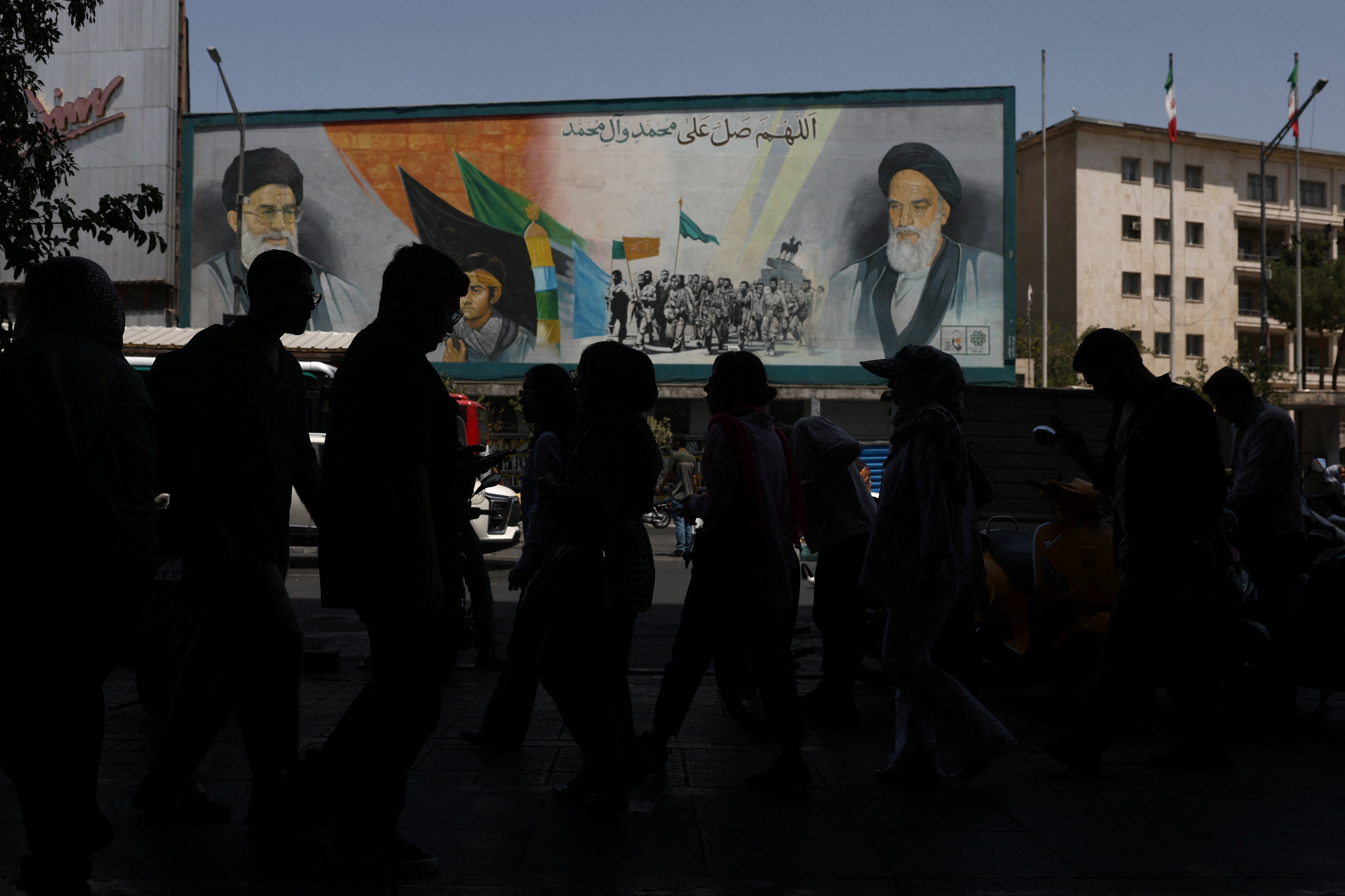 Iranians walk past a mural of Ayatollah Khomeini and late Ayatollah Khamenei on a Tehran street during the US-Iran war