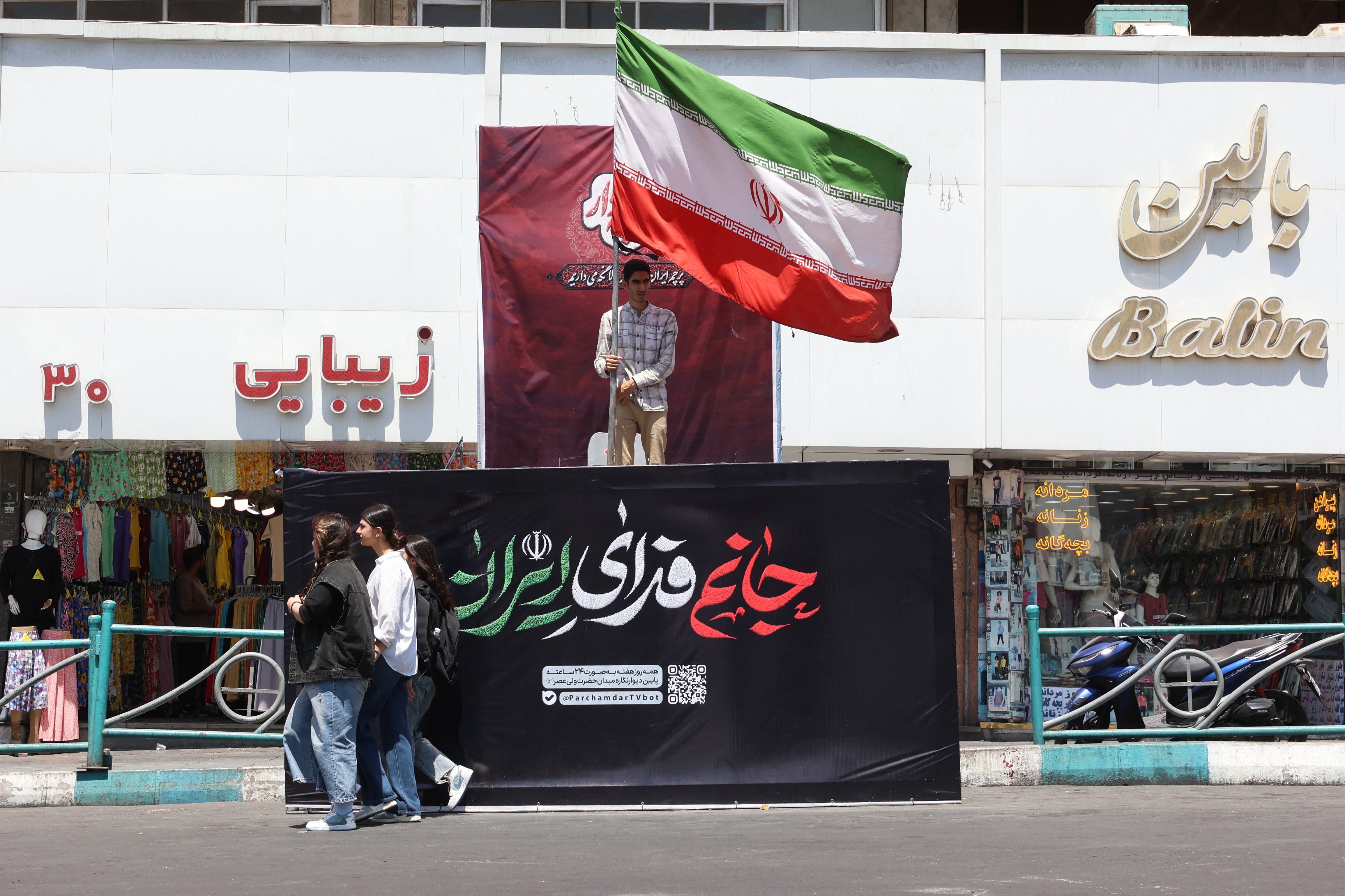 An Iranian man holds Iran's national flag at Valiasr Square in Tehran as the US-Iran conflict escalates and Vance accuses Israel of running influence campaign against Iran diplomacy
