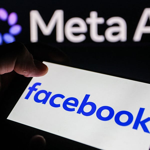 Hand holding smartphone displaying Facebook logo with Meta AI logo in the background