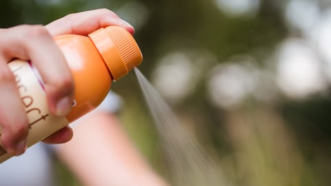 A person applying insect repellent spray to protect against West Nile virus mosquito bites