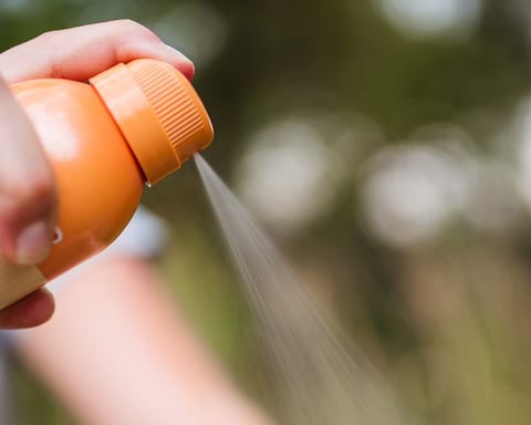A person applying insect repellent spray to protect against West Nile virus mosquito bites