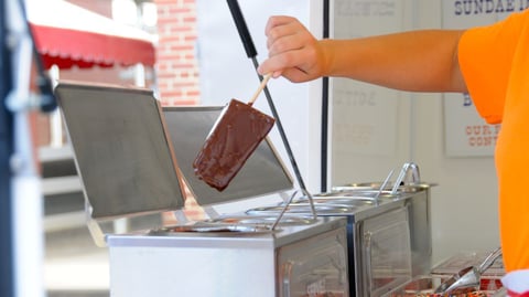 Vendor preparing frozen chocolate-dipped cheesecake on a stick at Ohio State Fair 2026