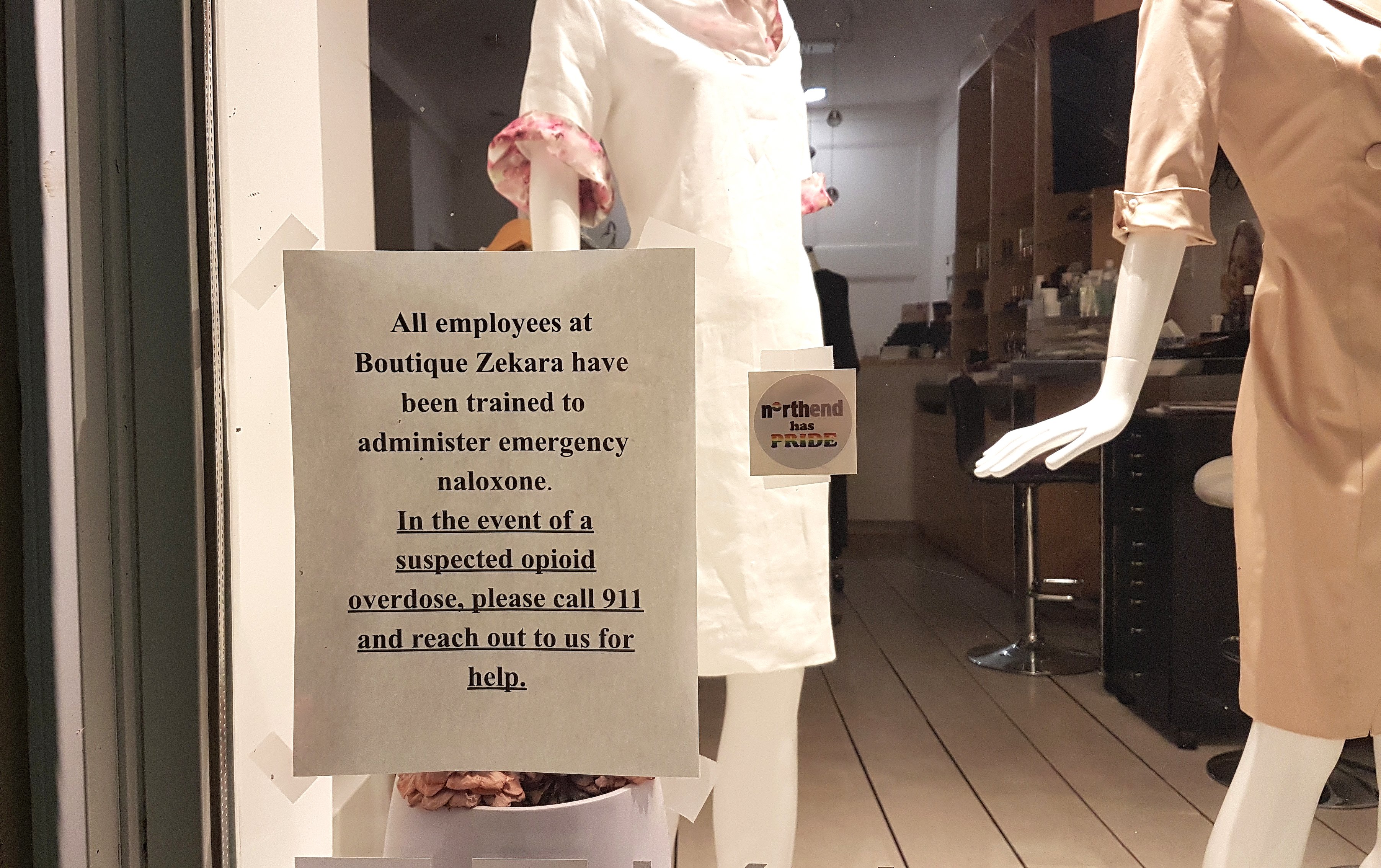 A store window sign in Halifax offering naloxone training and overdose response information, illustrating community harm reduction efforts during the opioid crisis