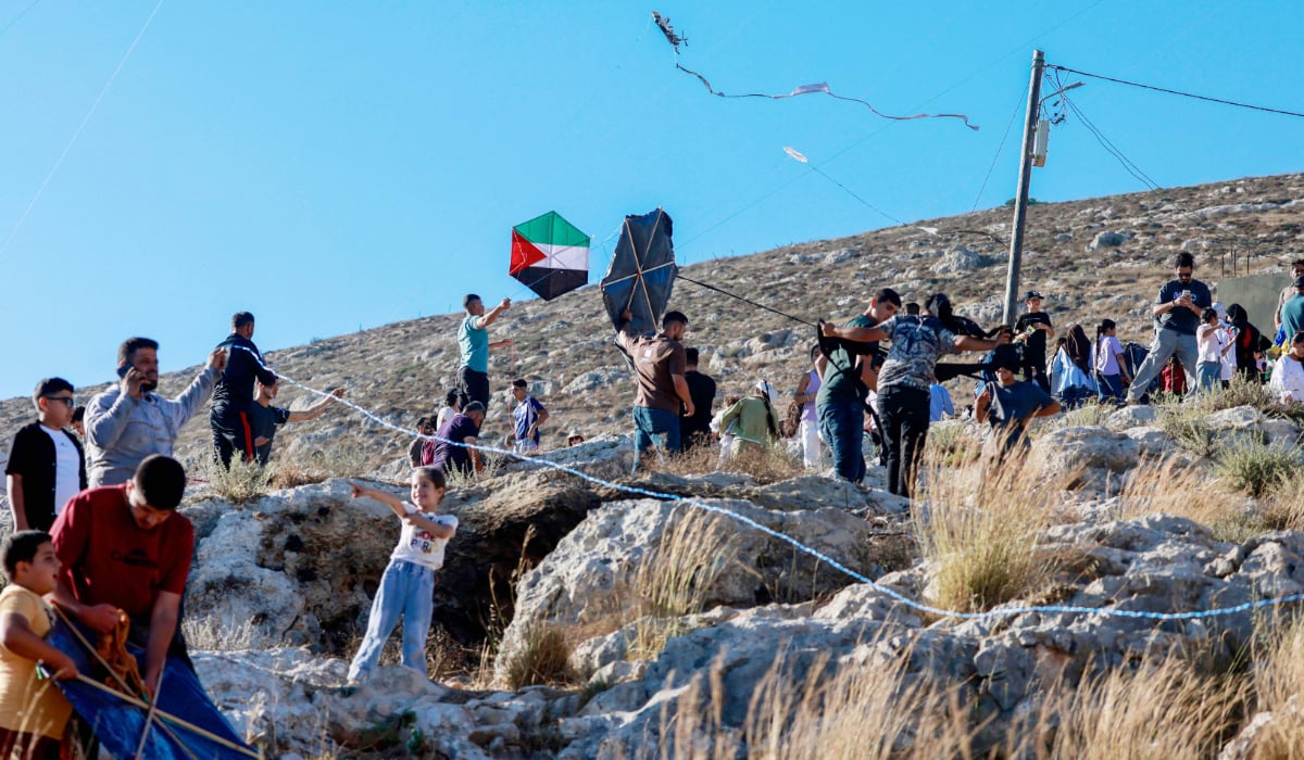 Palestinians and solidarity activists fly kites with Palestinian flag colors in Burin village, West Bank, toward the Israeli settlement of Har Bracha