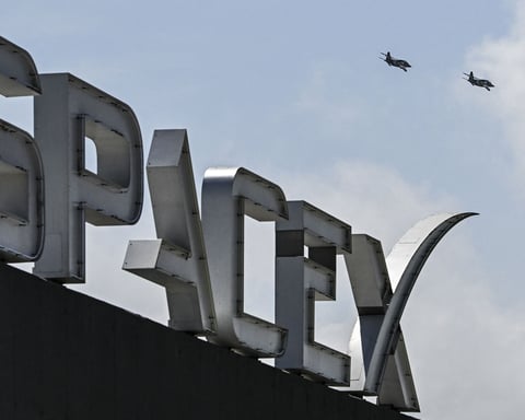 A fighter jet flies in formation near the SpaceX sign and Starship spacecraft at Starbase, Texas