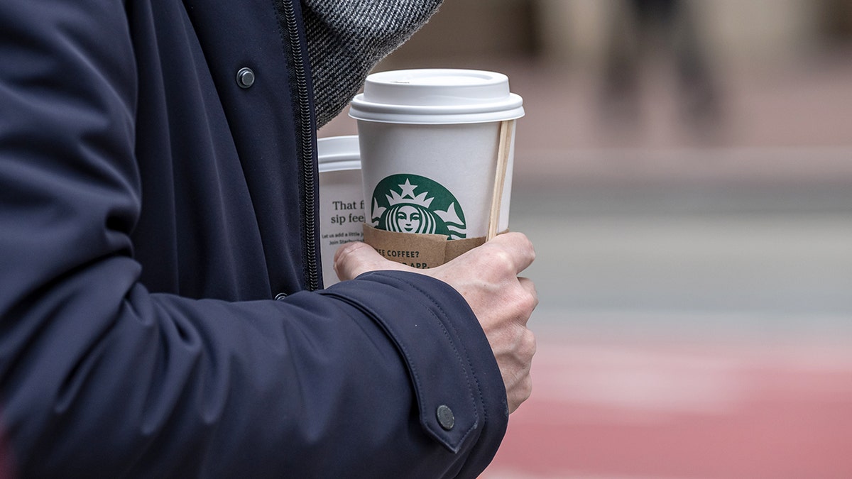 A customer holds a Starbucks coffee cup, reflecting the chain's improving customer traffic under CEO Brian Niccol's Back to Starbucks strategy