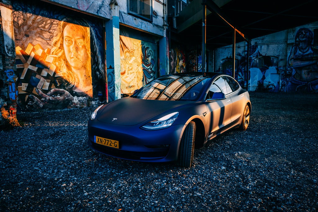 Dark matte blue Tesla Model 3 parked against an urban graffiti backdrop, Tesla Q2 2026