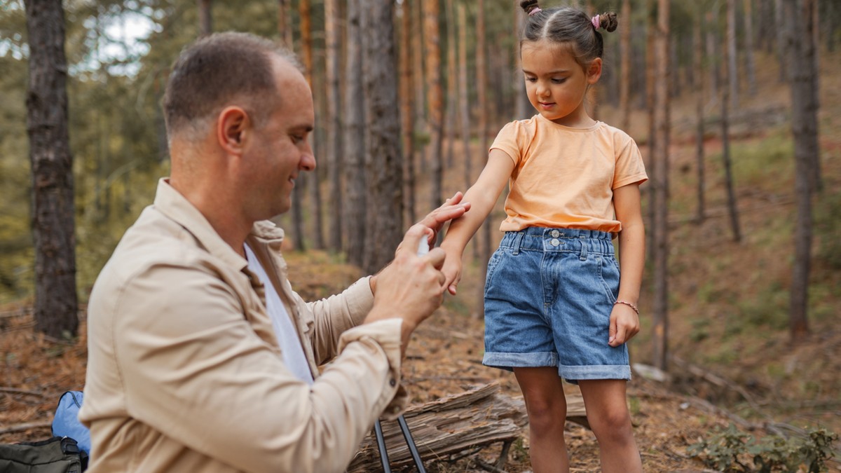 A father sprays EPA-registered tick repellent on his daughter before a hike in a wooded area