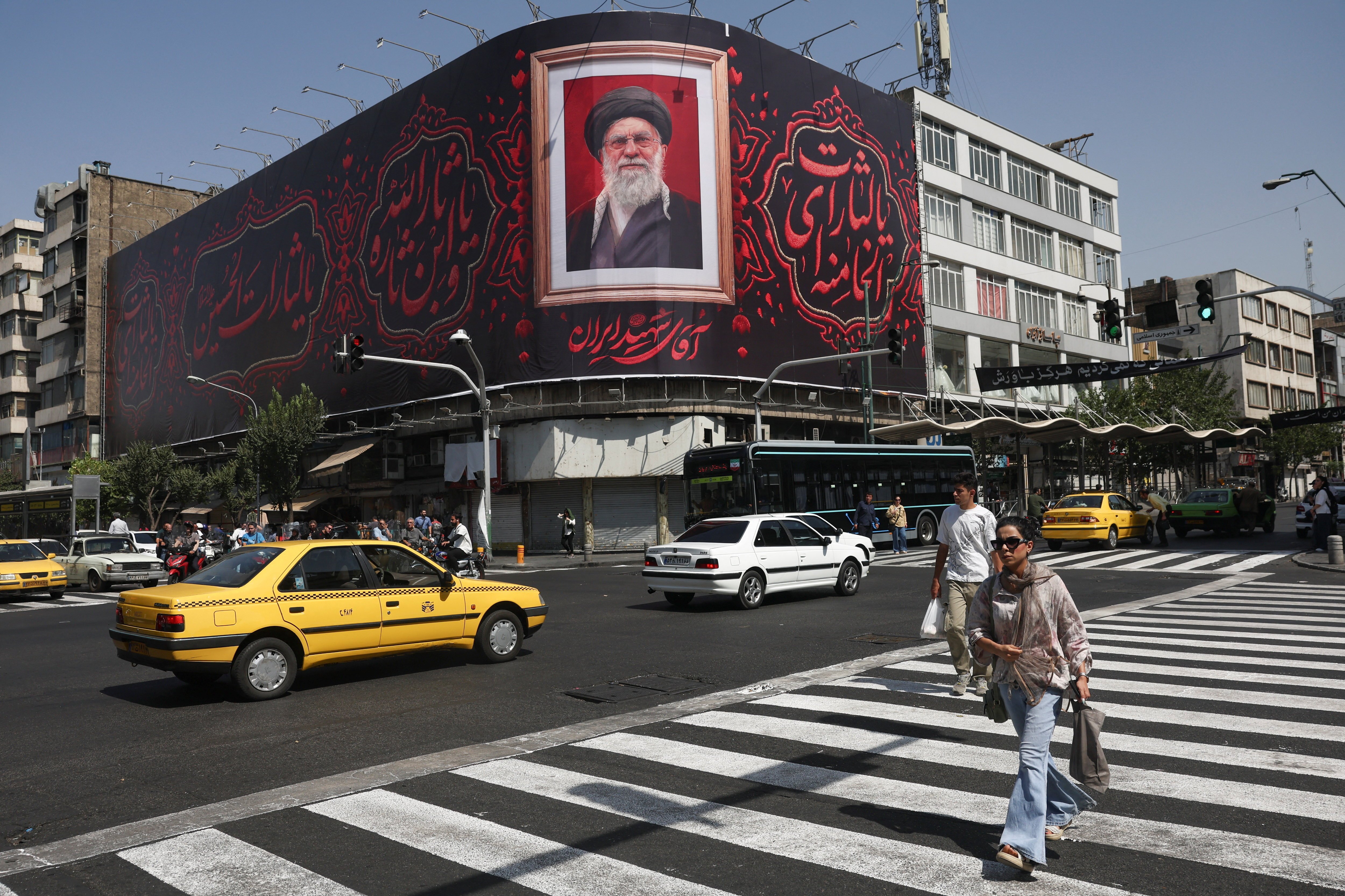 Residents walk past a billboard of late Supreme Leader Ali Khamenei in Tehran, Iran, July 13, 2026, as the US and Iran resumed military hostilities