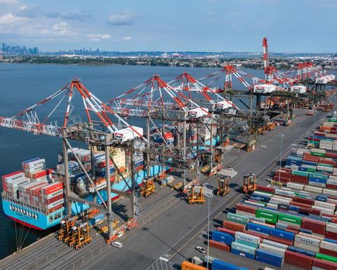 Container ships unload imported cargo at a US port as AI-driven capital goods imports push the May 2026 trade deficit higher.