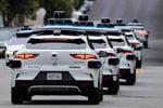 A line of Waymo autonomous vehicles navigating through San Francisco's North Beach neighborhood during Fourth of July celebrations