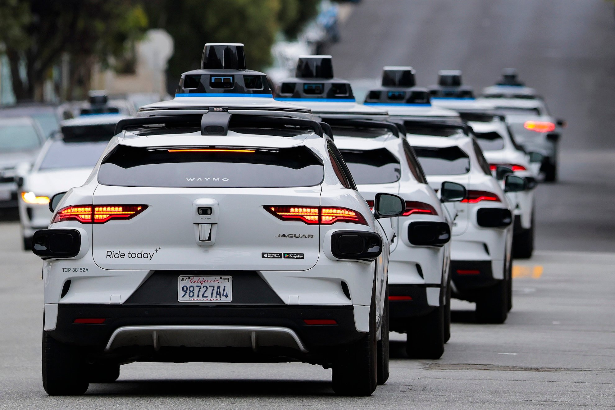 A line of Waymo autonomous vehicles navigating through San Francisco's North Beach neighborhood during Fourth of July celebrations
