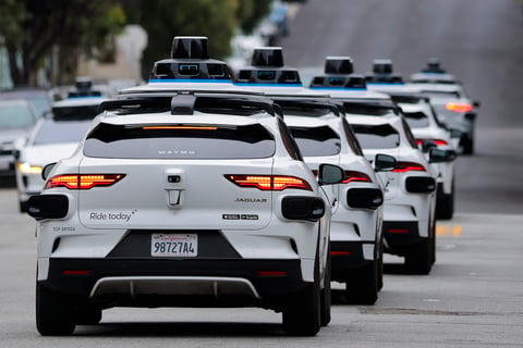 A line of Waymo autonomous vehicles navigating through San Francisco's North Beach neighborhood during Fourth of July celebrations