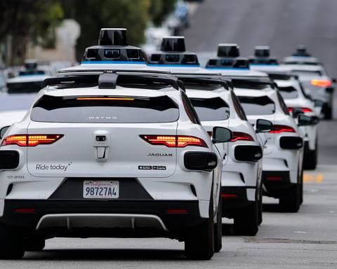 A line of Waymo autonomous vehicles navigating through San Francisco's North Beach neighborhood during Fourth of July celebrations