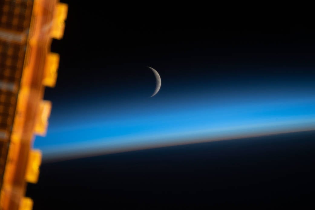 A waxing crescent moon photographed just above the curve of Earth's limb from the International Space Station