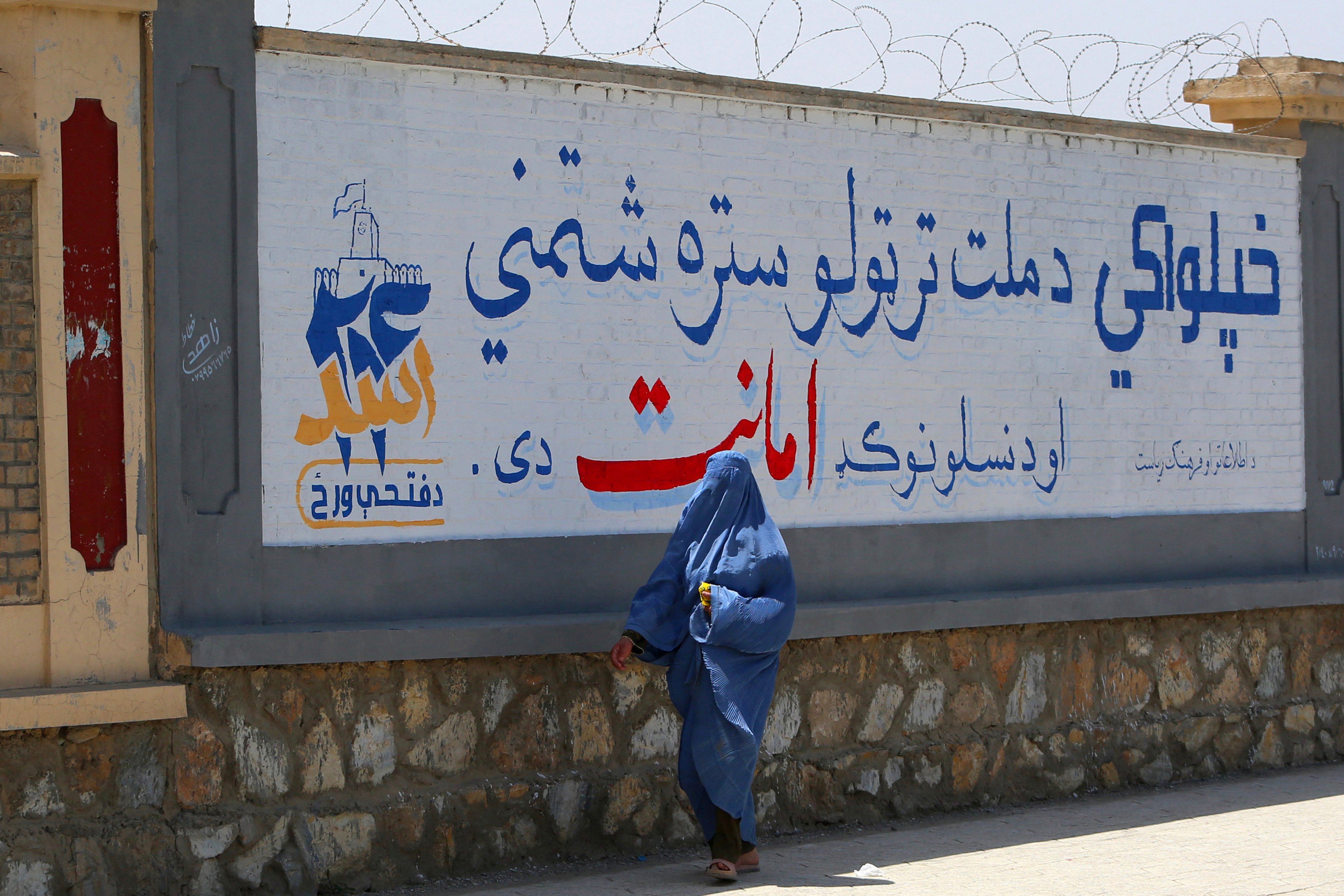 An Afghan woman in a burqa walks past a mural marking the fifth anniversary of Taliban rule in Ghazni province, Afghanistan
