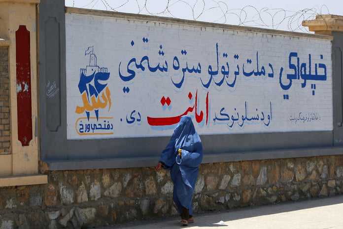 An Afghan woman in a burqa walks past a mural marking the fifth anniversary of Taliban rule in Ghazni province, Afghanistan