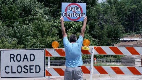 A protester stands near road barriers at the proposed White Cloud Acres AI data center site in Nodaway County Missouri