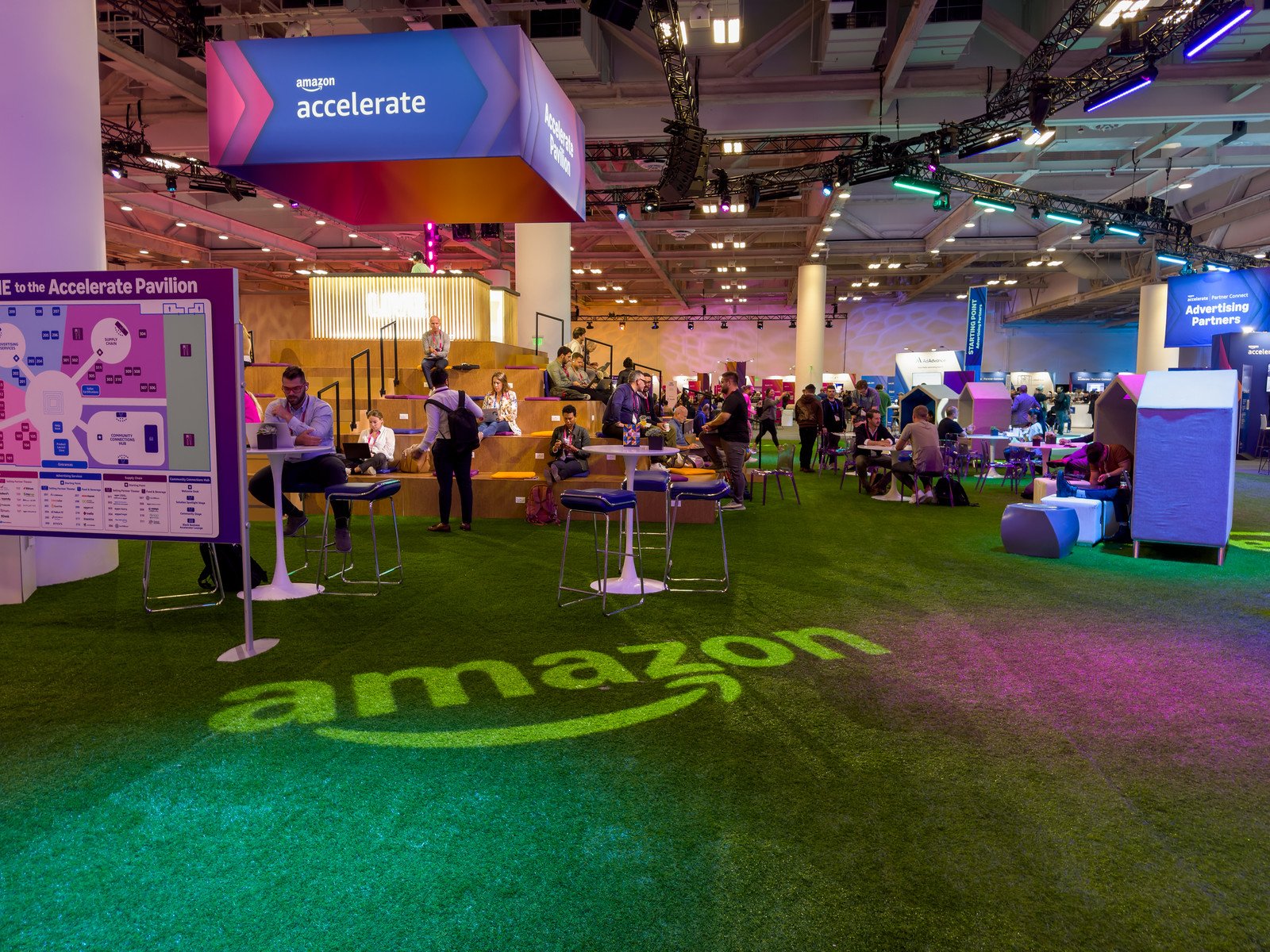 Amazon Accelerate conference pavilion floor showing Amazon logo in green lighting with attendees networking