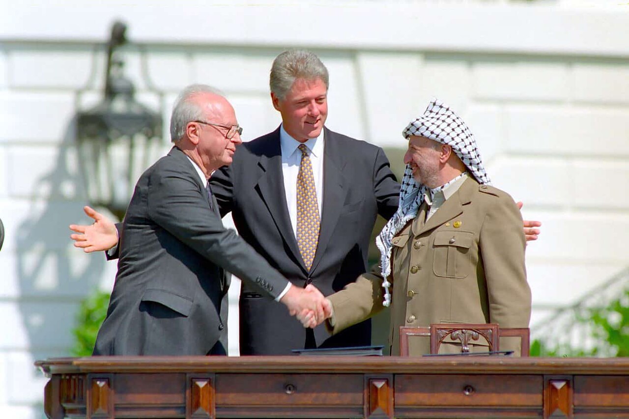 Yitzhak Rabin shaking hands with Yasser Arafat as Bill Clinton stands between them with arms outstretched on the White House lawn