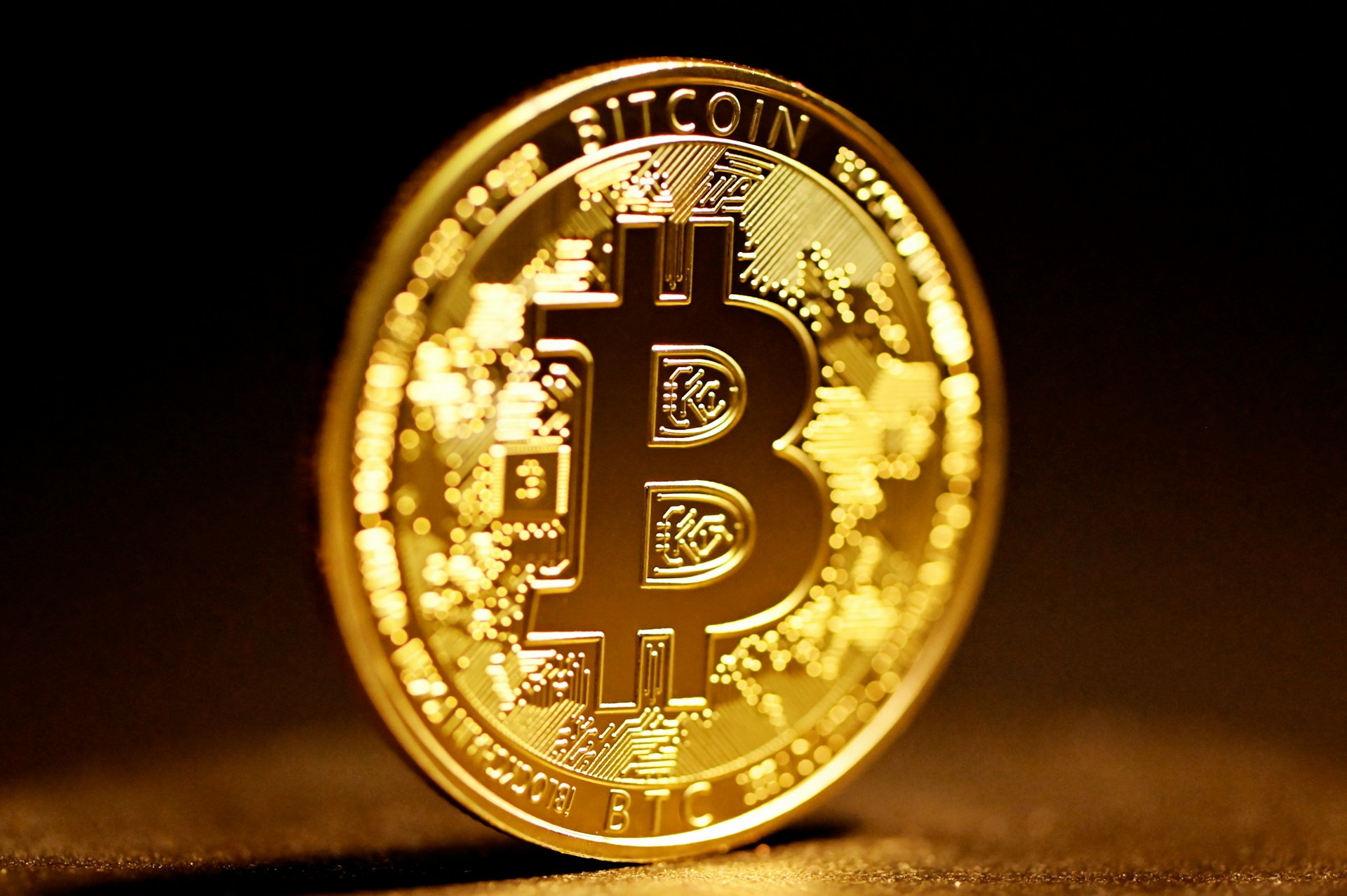 Close-up of a physical gold Bitcoin coin on a dark background with warm bokeh lighting