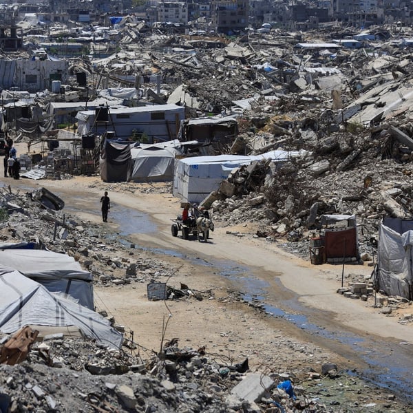 Displacement tents pitched among the rubble of a flattened Gaza neighbourhood, with people and a donkey cart on a dirt track running through it