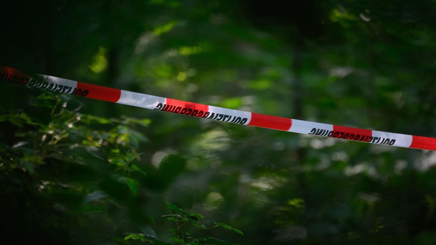 Red and white German police cordon tape strung across dense green woodland