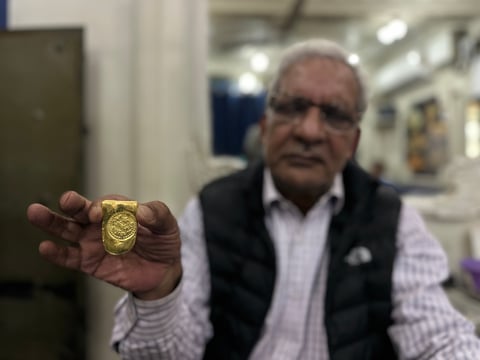 A goldsmith holds a tray of pure gold ornaments in a workshop, illustrating the gold rate today in India