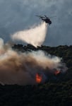 Firefighting helicopter drops water over wildfire smoke billowing near Porto Germeno resort along the Gulf of Corinth in Greece, August 2026