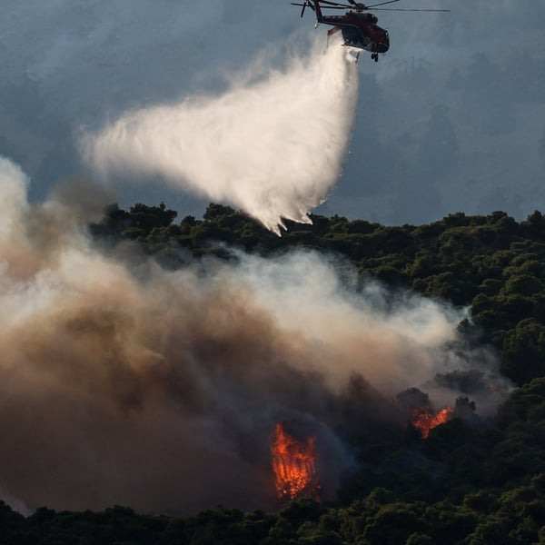Firefighting helicopter drops water over wildfire smoke billowing near Porto Germeno resort along the Gulf of Corinth in Greece, August 2026