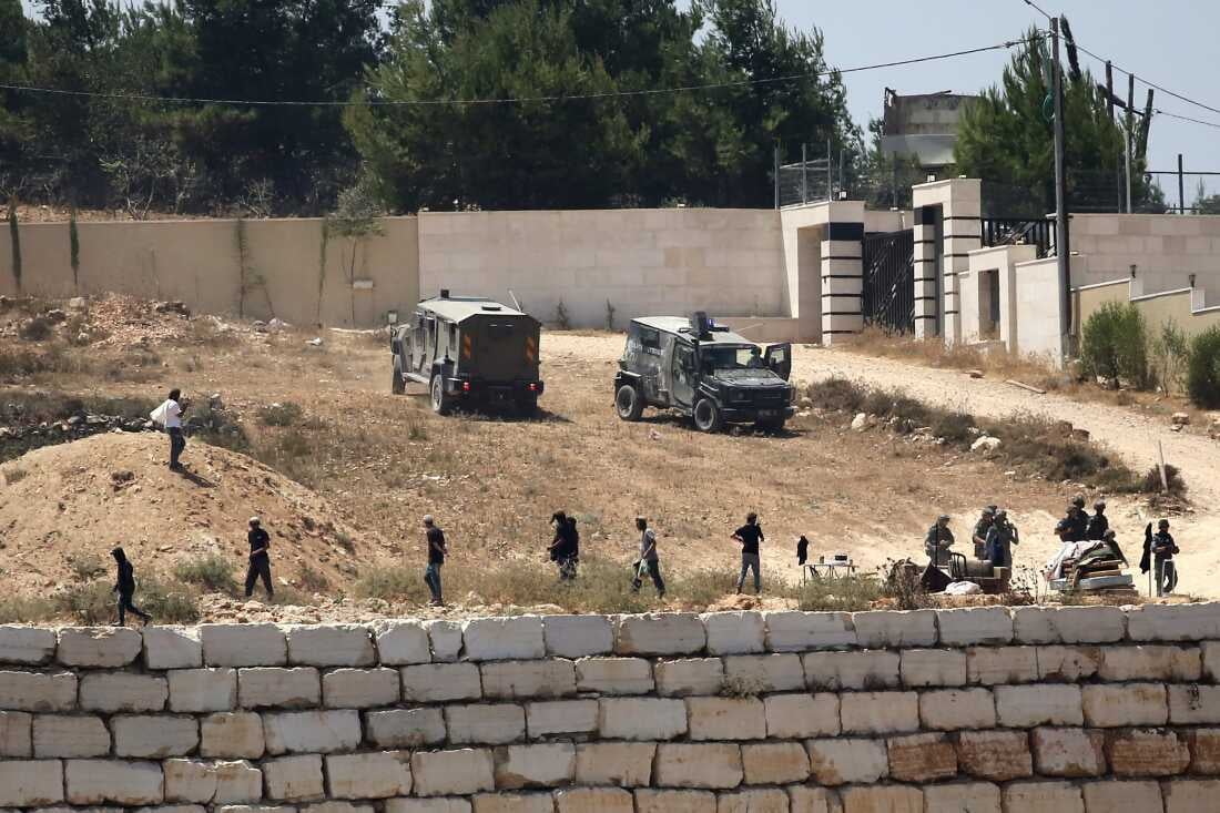 Israeli soldiers standing guard next to settlers outside Palestinian homes in Qusra village, West Bank
