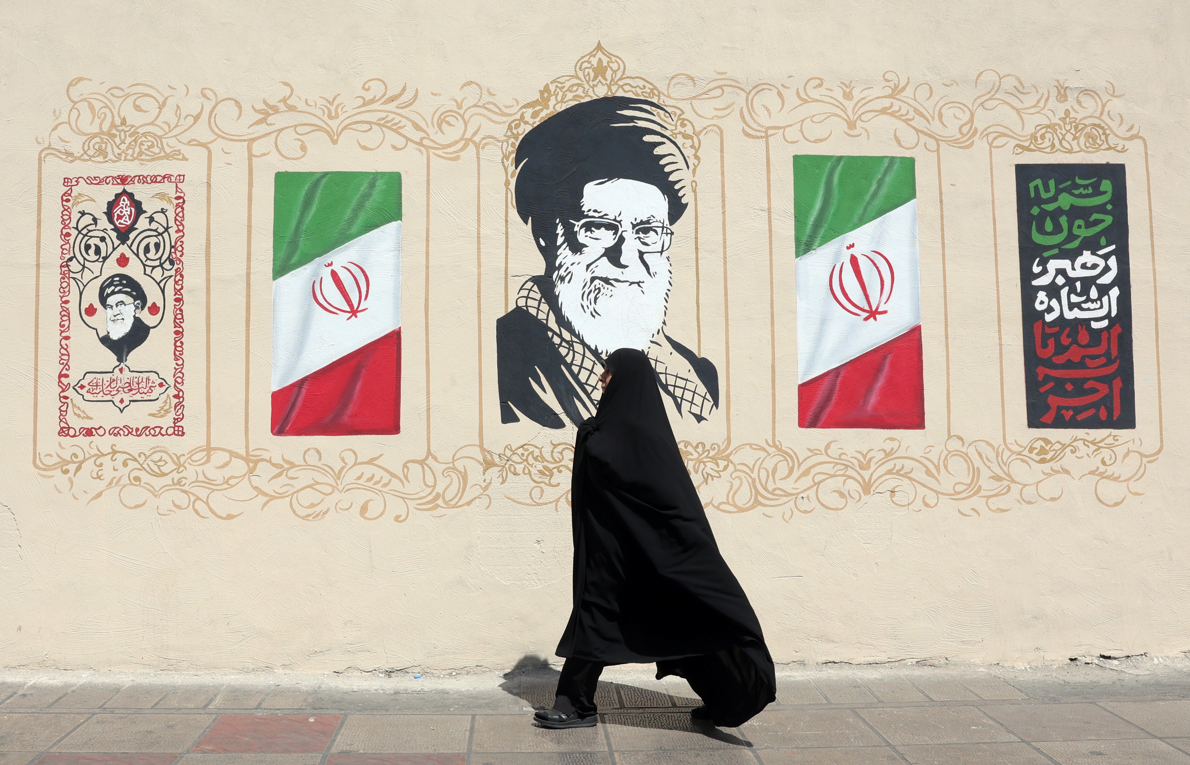 A woman walks in Tehran next to a wall painting of Ayatollah Khamenei as Iran faces US sanctions under Operation Economic Outcast