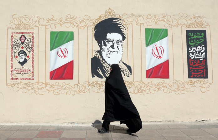 A woman walks in Tehran next to a wall painting of Ayatollah Khamenei as Iran faces US sanctions under Operation Economic Outcast
