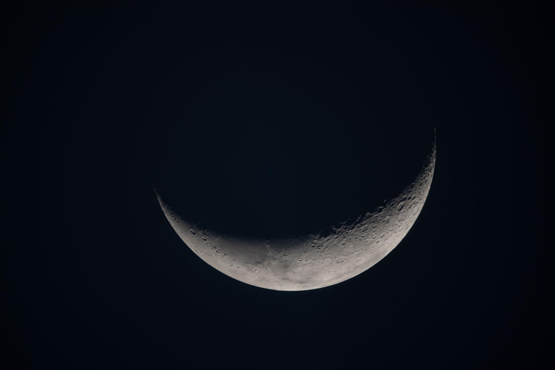A crescent moon against black space, showing the terminator line where low sunlight throws long shadows across the lunar surface