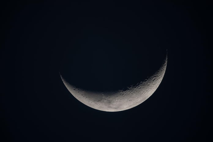 A crescent moon against black space, showing the terminator line where low sunlight throws long shadows across the lunar surface