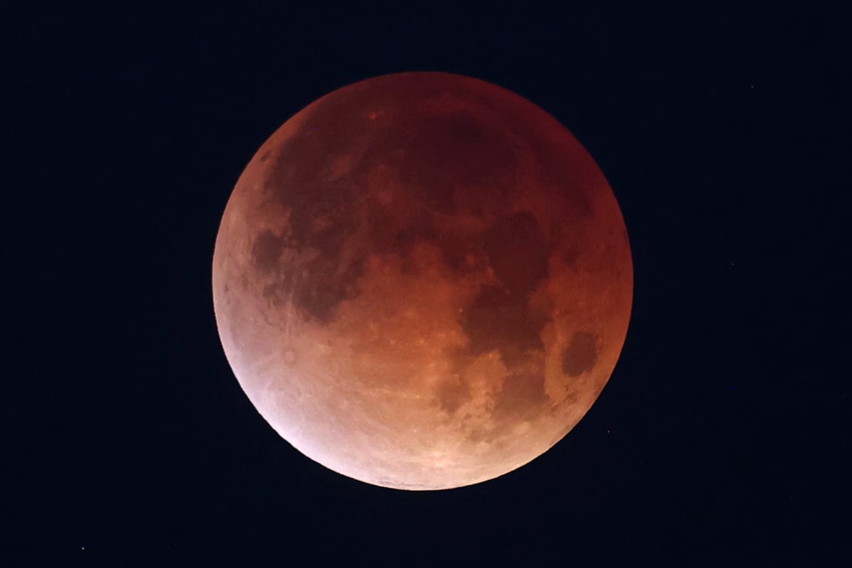 A totally eclipsed moon glowing deep copper red against a black sky