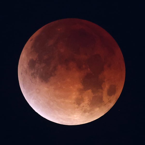 A totally eclipsed moon glowing deep copper red against a black sky