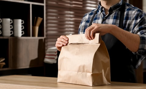 A restaurant worker hands a takeout bag across a counter, illustrating New Jersey's Skip the Stuff law requiring utensils to be opt-in