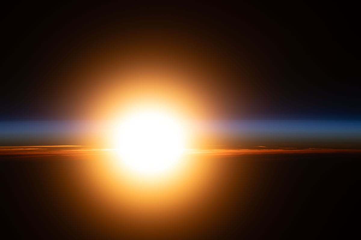 A bright orange sunburst rising through Earth's atmosphere during an orbital sunrise seen from the International Space Station