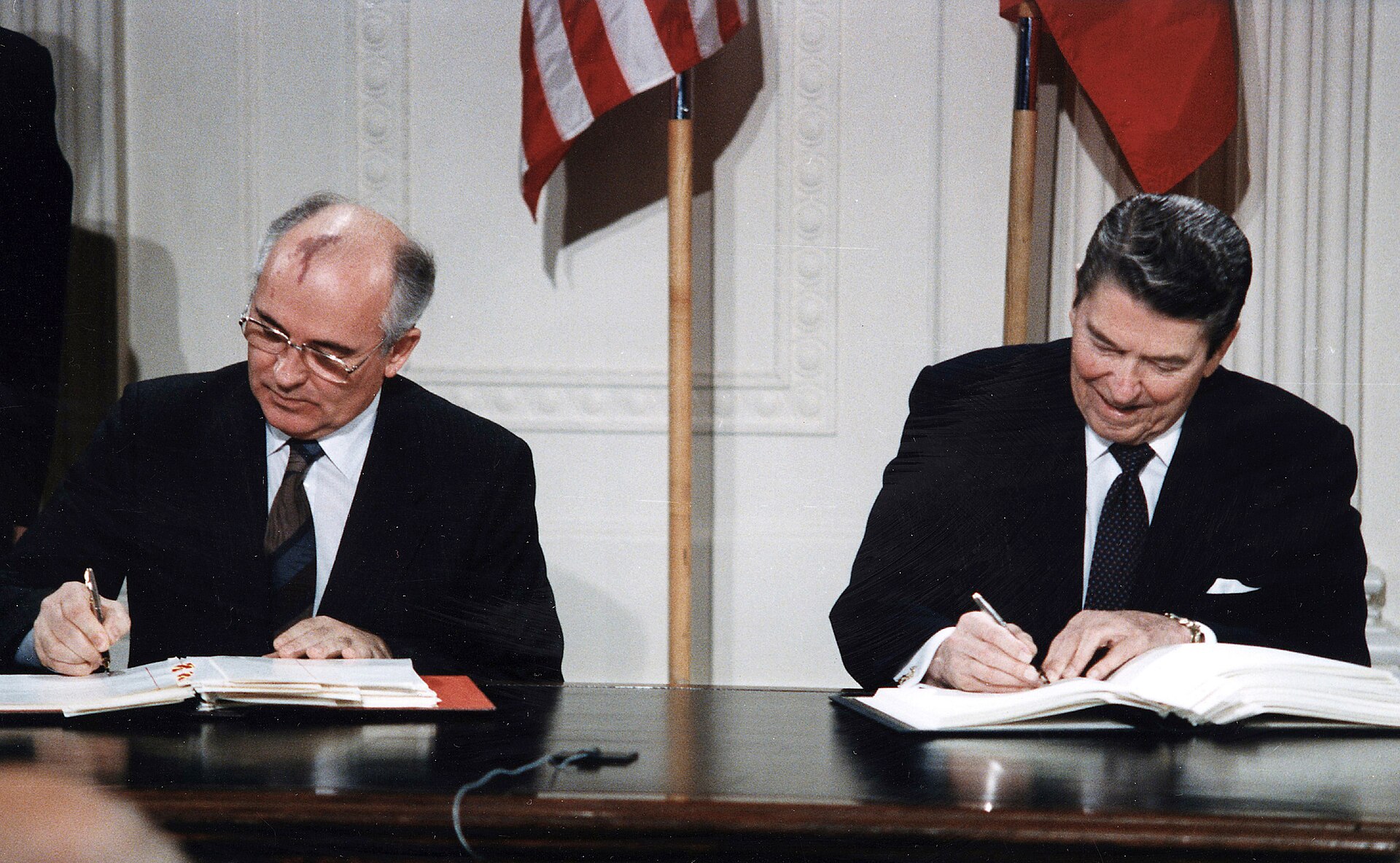 Mikhail Gorbachev and Ronald Reagan seated at a table signing the Intermediate-Range Nuclear Forces Treaty in the White House East Room