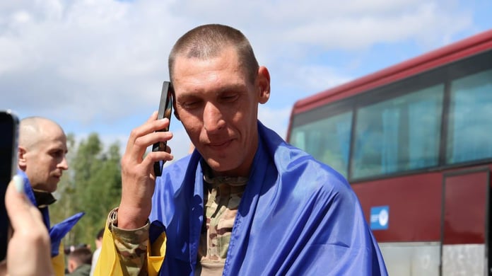 A freed Ukrainian serviceman wrapped in a national flag makes a phone call after the August 19 prisoner exchange