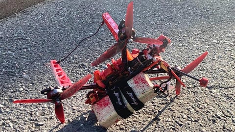 A small quadcopter drone covered in red paint lies on tarmac with two white blocks strapped beneath it, recovered near the Russian embassy in Stockholm