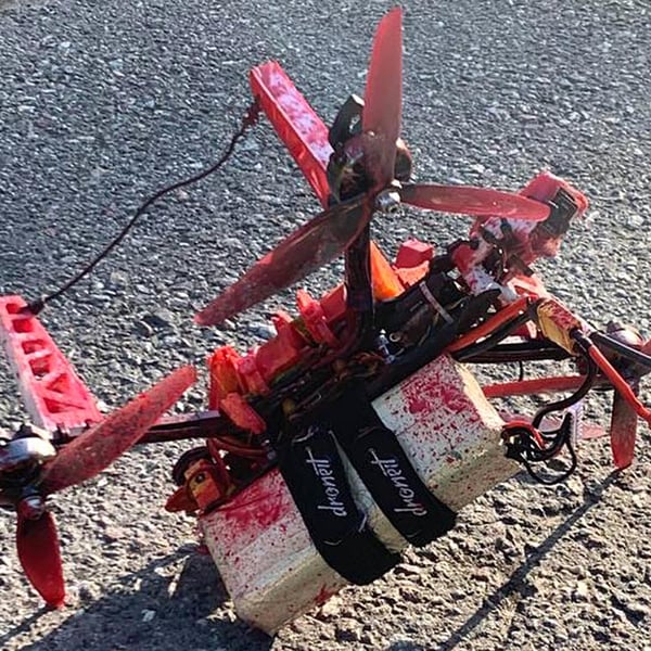 A small quadcopter drone covered in red paint lies on tarmac with two white blocks strapped beneath it, recovered near the Russian embassy in Stockholm