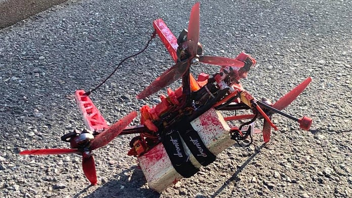 A small quadcopter drone covered in red paint lies on tarmac with two white blocks strapped beneath it, recovered near the Russian embassy in Stockholm