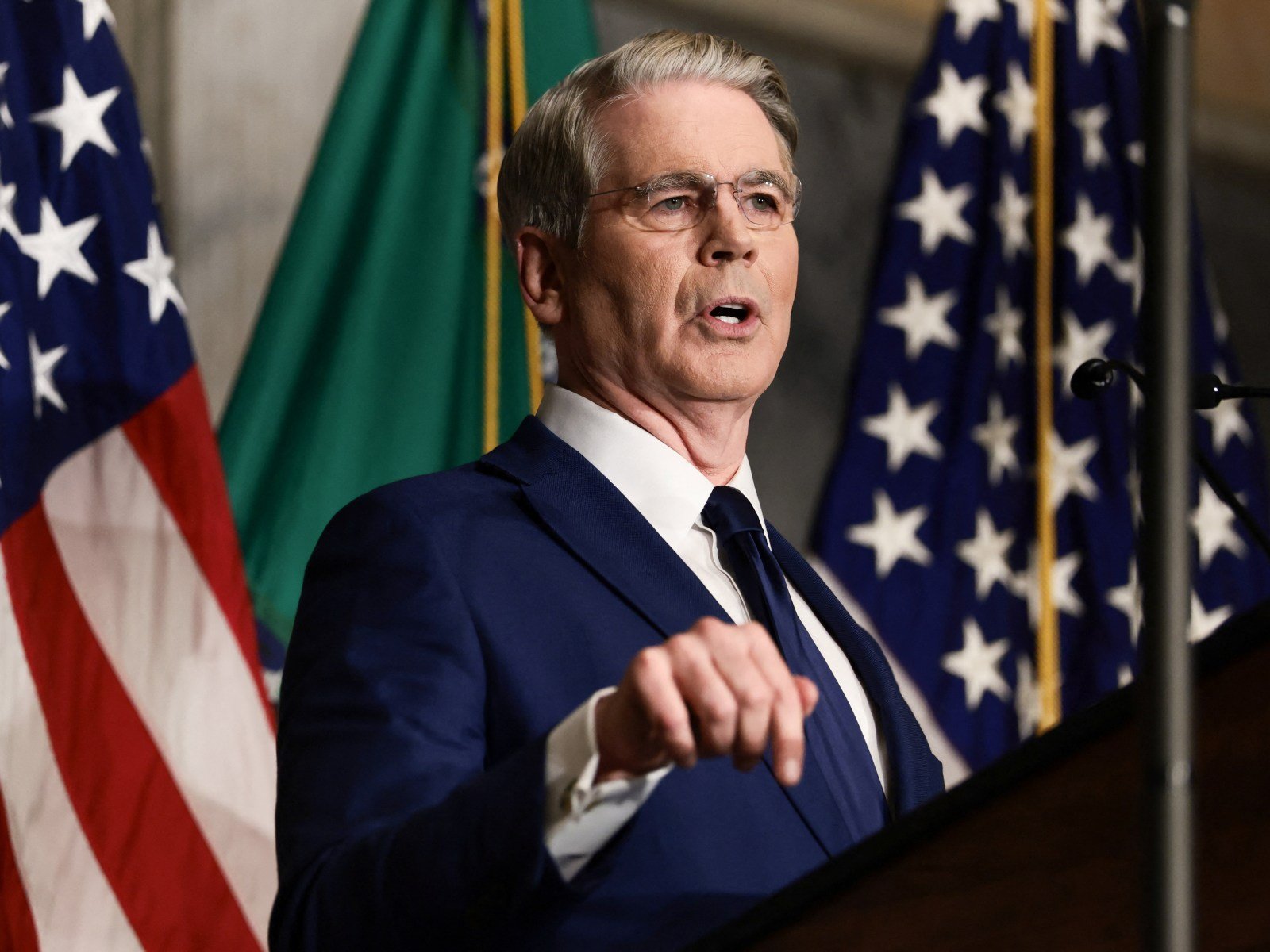 US Treasury Secretary Scott Bessent points while speaking at a podium in front of American flags and the Treasury Department flag