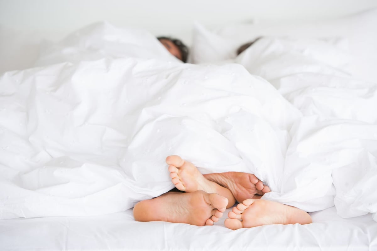 Couple's feet in bed illustrating research on sex frequency and relationship happiness