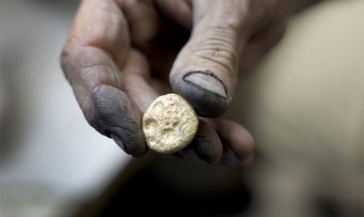 A metalworker's blackened hand holding a small freshly cast button of precious metal, illustrating the silver rate today at Rs 2,60,000 a kilogram