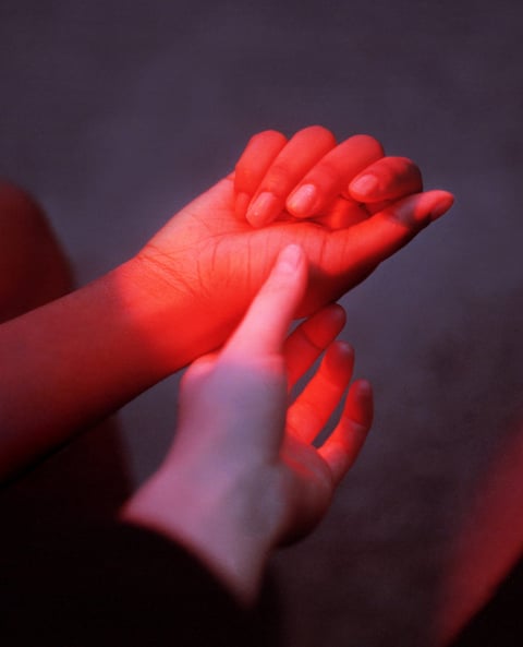 Two hands reaching for each other in red light representing intimacy and sexual desire in a relationship