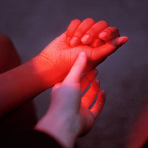 Two hands reaching for each other in red light representing intimacy and sexual desire in a relationship